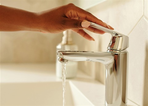 A woman lifts the handle of a bathroom faucet.